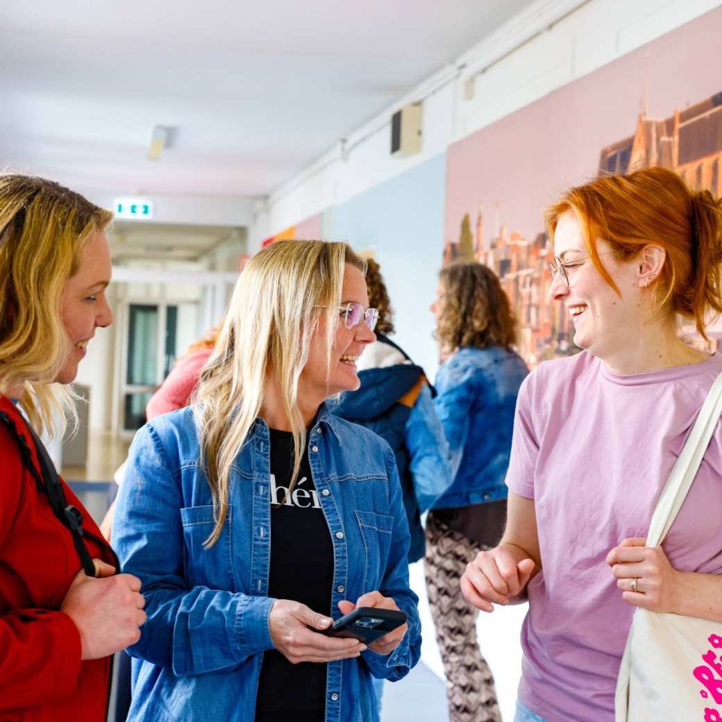 Vrouw laat iets zien op haar mobiel tijdens de cursus acute pijn service. Andere studenten moeten lachen.