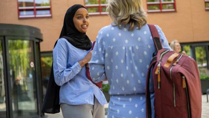 Student met hoofddoek praat buiten met docent, studentbegeleiding, bij K33.