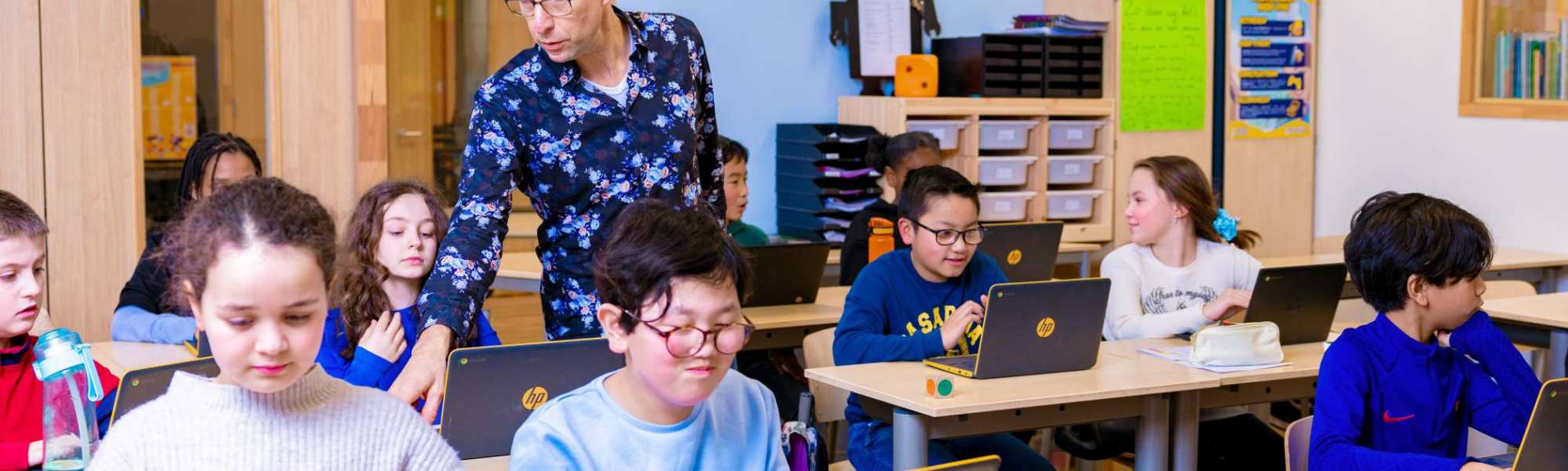 Groep 5,6,7 op de school Da Vince. De leerlingen zitten in de klas achter de laptop terwijl de leraar rond loopt. 