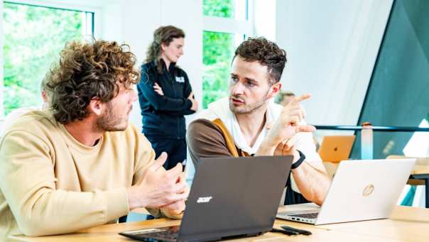 2 studenten die een module volgen overleggen met elkaar in een klaslokaal.