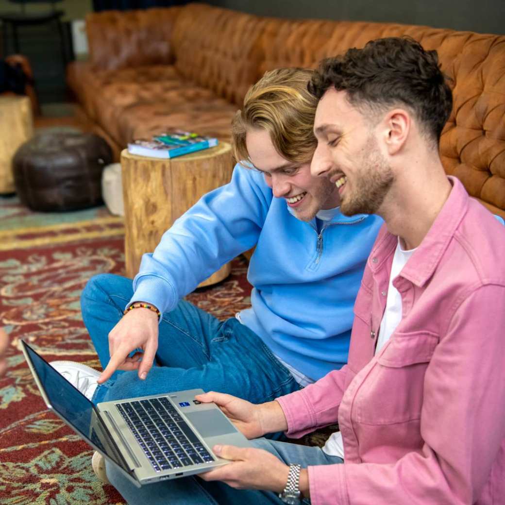 Twee studenten werken samen achter de laptop en kijken lachend naar het scherm.