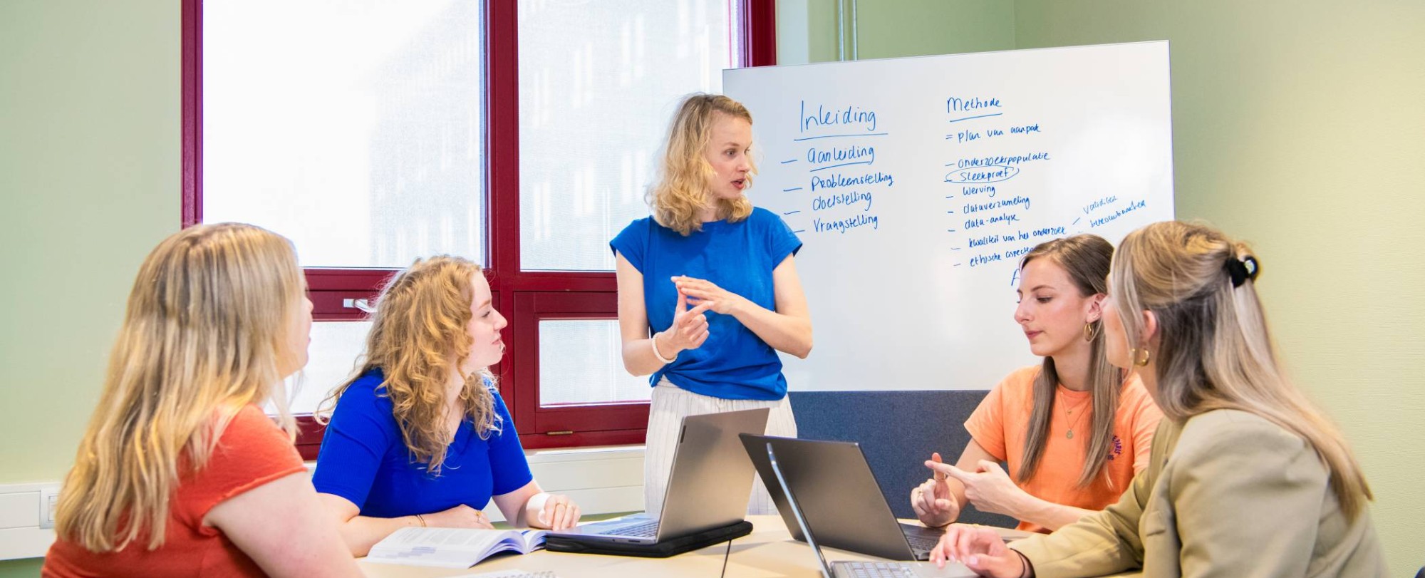 Groep studenten in gesprek met docent Verpleegkunde bij bord