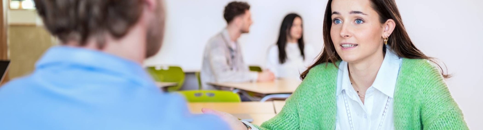 Studenten van Leraar Economie werken aan een groepsopdracht en de docent kijkt toe.