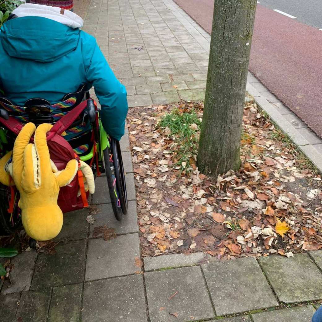 Foto van student in een rolstoel, op weg naar de campus. Hij rijdt op een te smalle stoep.