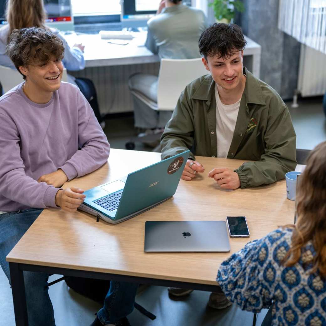 Studenten zitten in een klas en werken samen aan tafel, ze hebben plezier. 