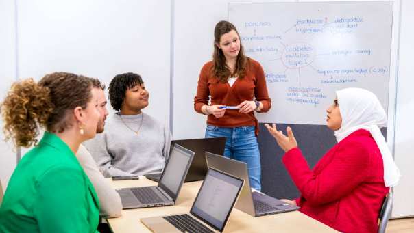 Docent staat voor een whiteboard en luistert naar een vraag van een leerling over diabetes.