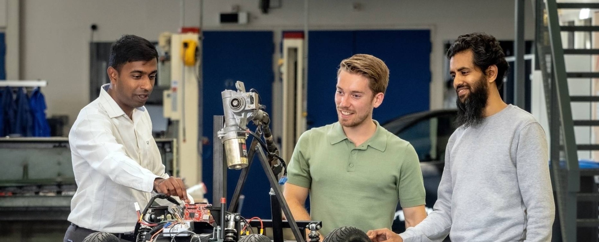 Een docent van de Master Engineering Systems Cyber Physical Systems legt het MORE-project , de scootmobiel, uit aan twee studenten.