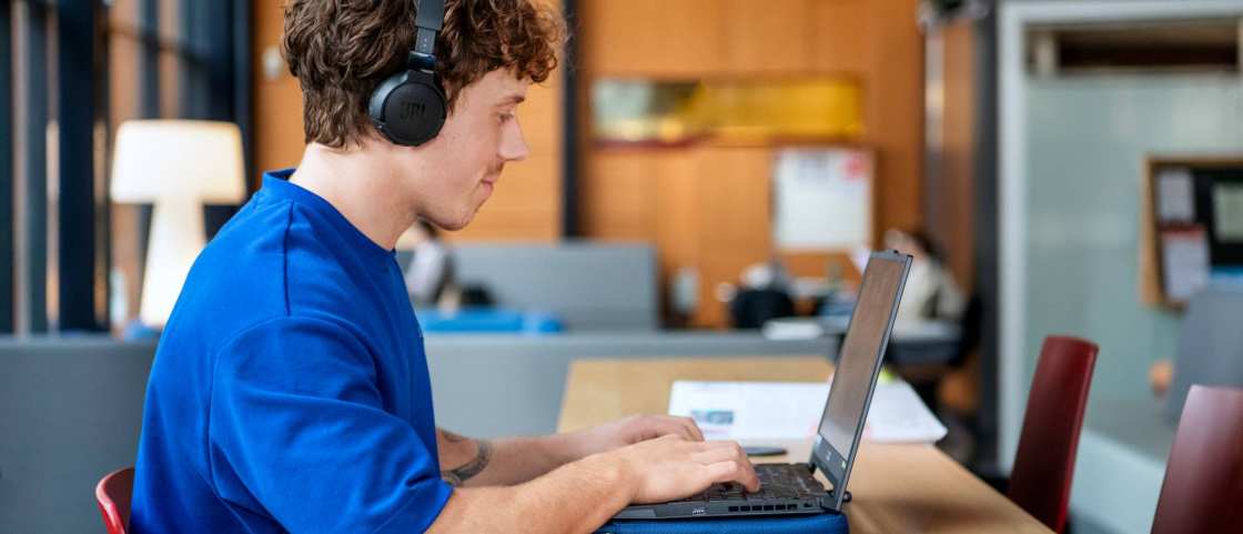 Student met koptelefoon werkt achter computer.