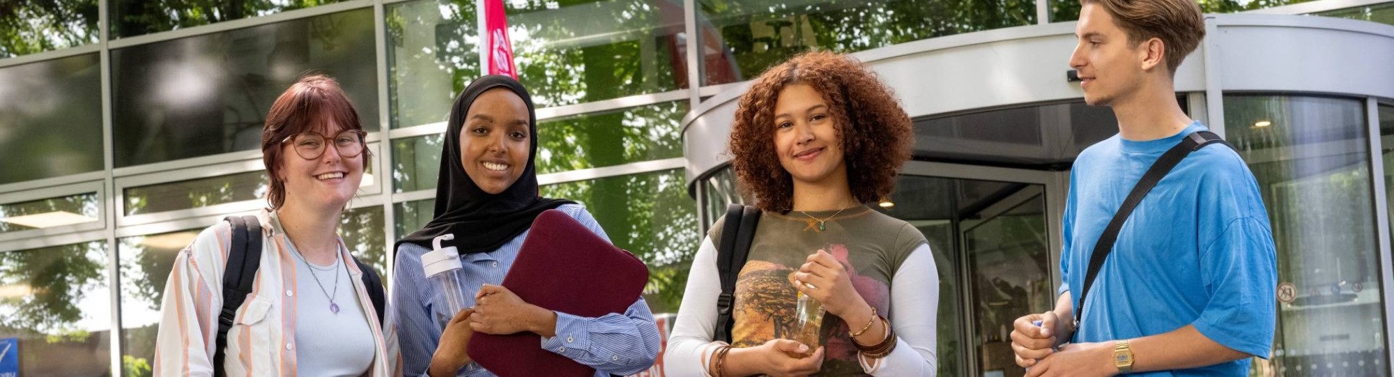 Vier studenten staan bij gebouw LvS10 bij draaideur, buiten. Op een rijtje. 