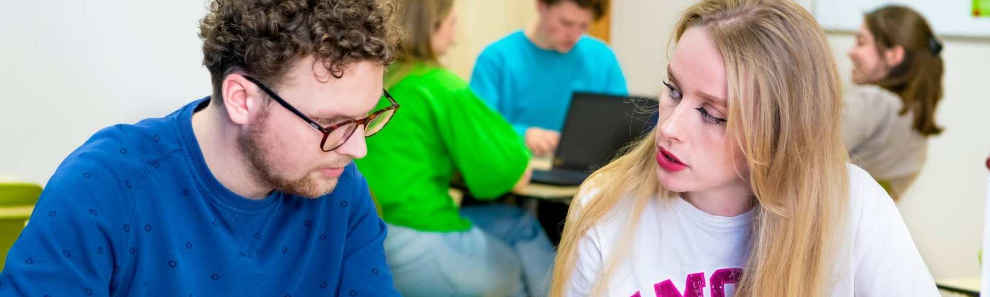 Twee studenten spelen een kaartspel met blauwe kaartjes in een gekleurd leraar Duits lokaal.
