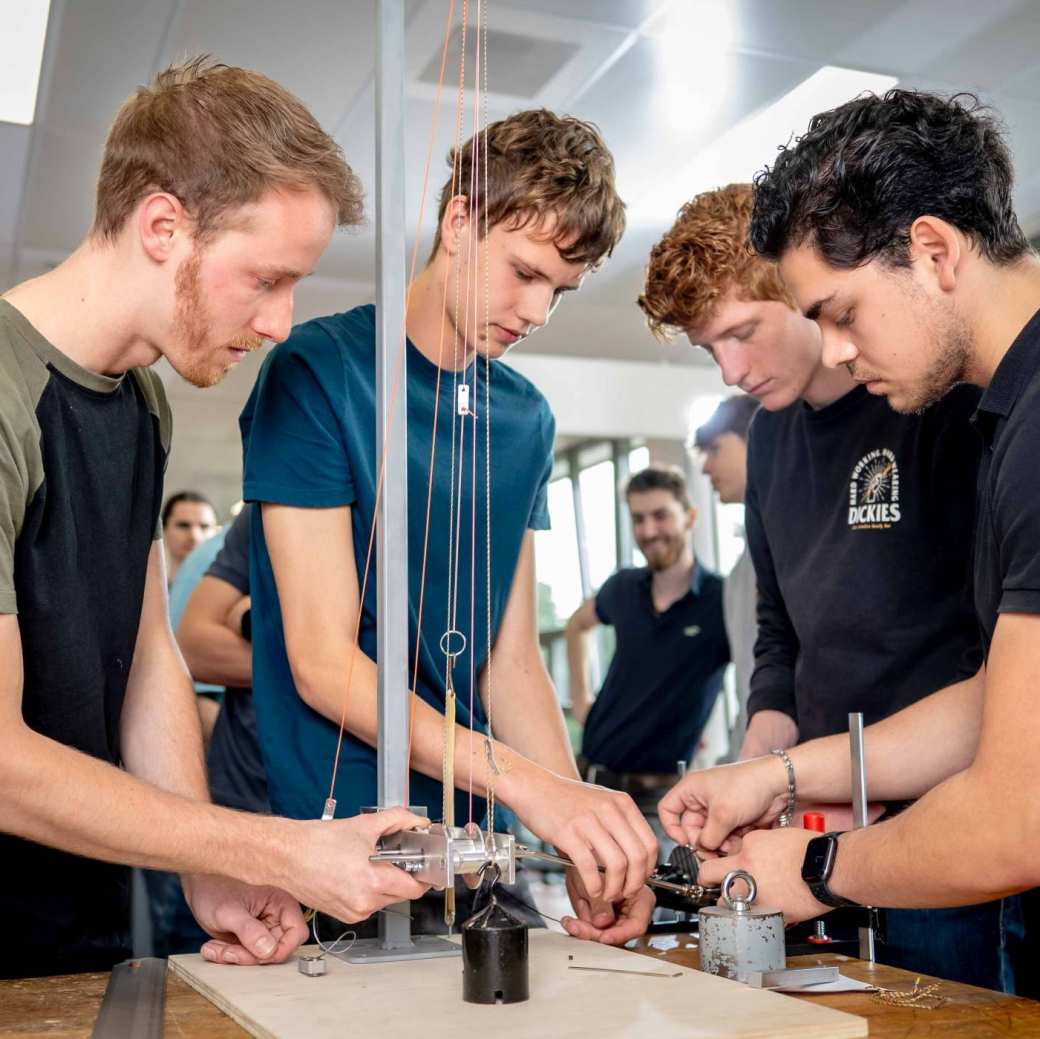 Vier studenten werktuigbouwkunde doen tests met een katrol en gewichten.