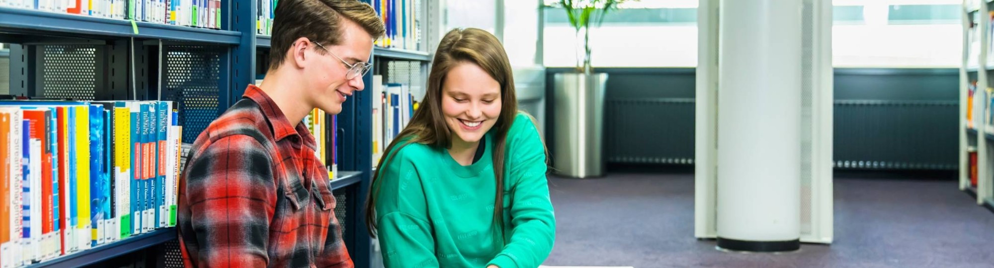 jongen en meisje studeren samen op de grond in studiecentrum en zij wijst iets aan