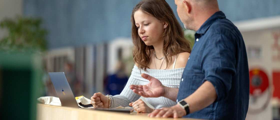 Een docent heeft een gesprek met een student in de hal van gebouw R26, studentbegeleiding. 