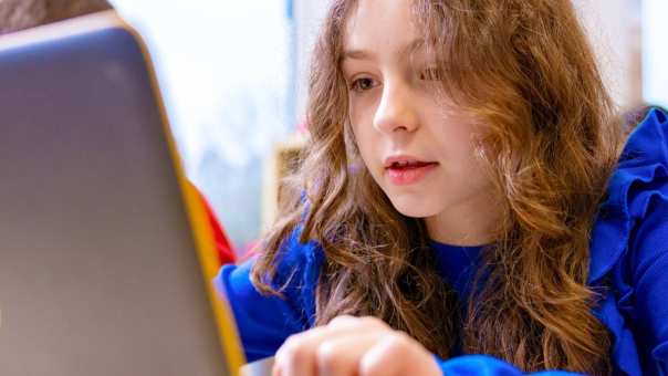 Groep 5,6,7 op de school Da Vince. Een leerling is aan het werk achter haar laptop in de klas. 