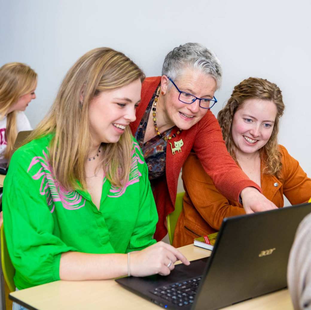 Docent kijkt mee bij twee leerlingen achter de laptop.