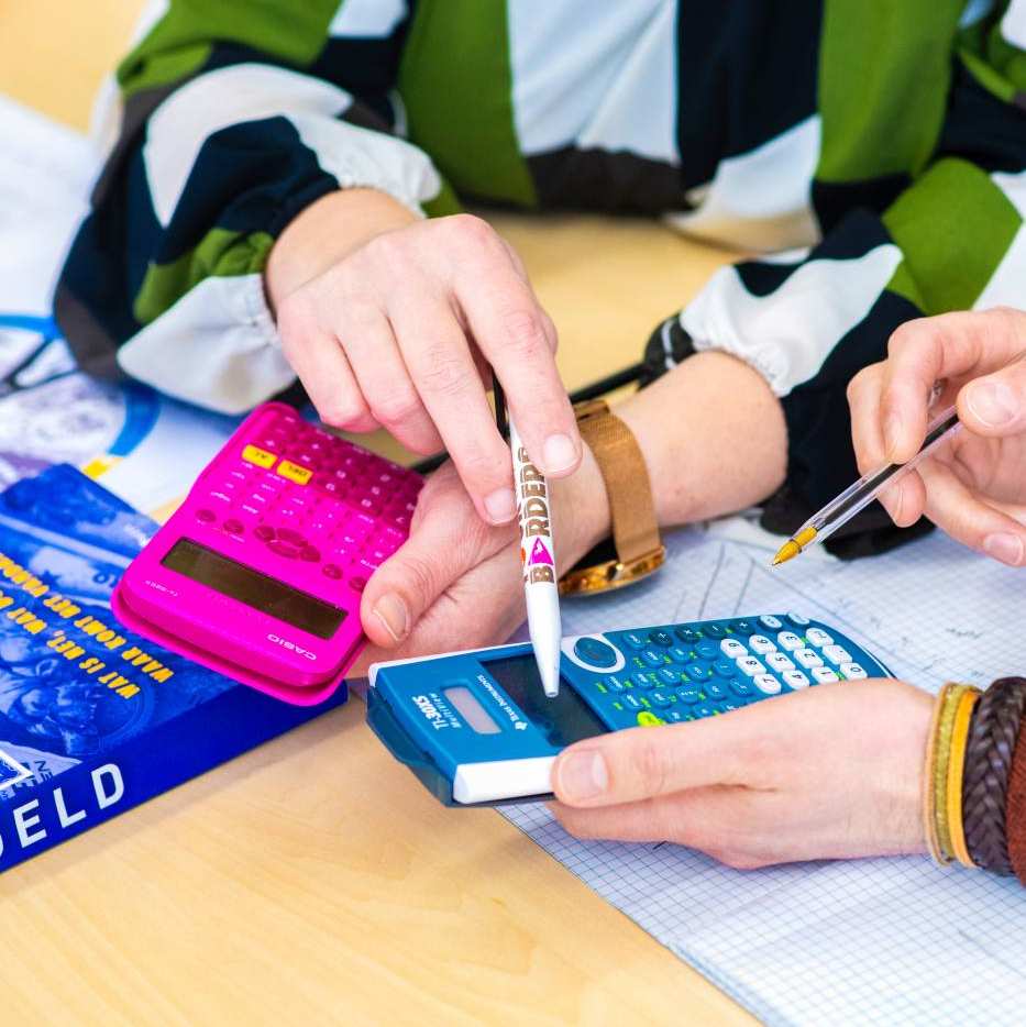 Studenten Leraar Economie tikken een som in op de rekenmachine.