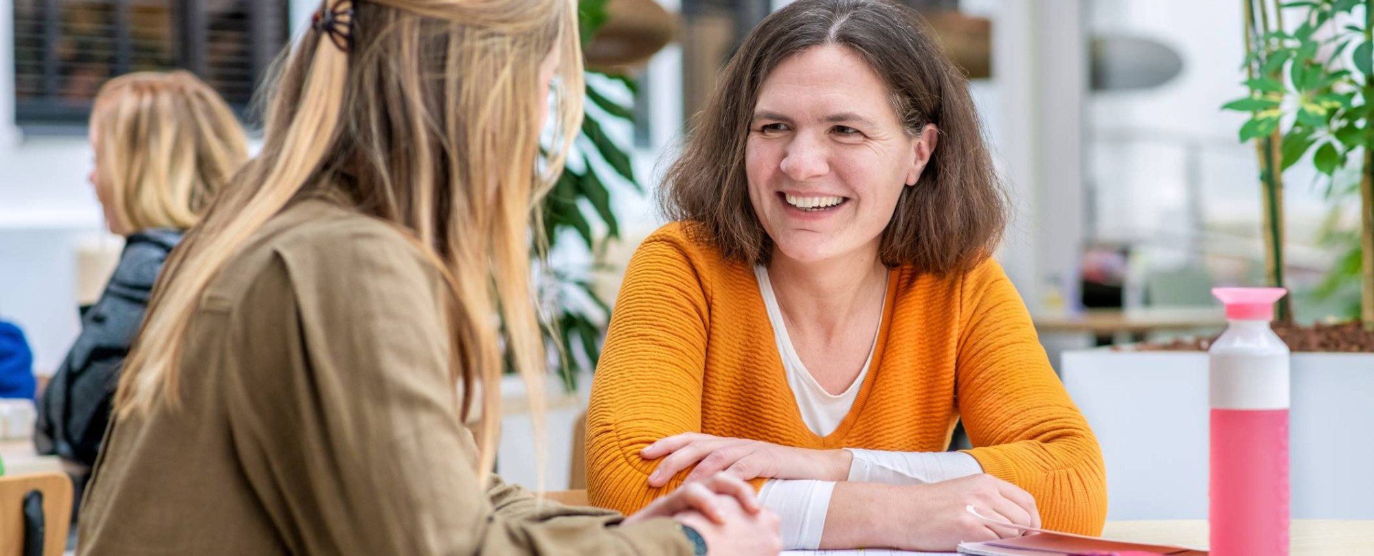 Vrouw in oranje trui lacht naar medestudent.