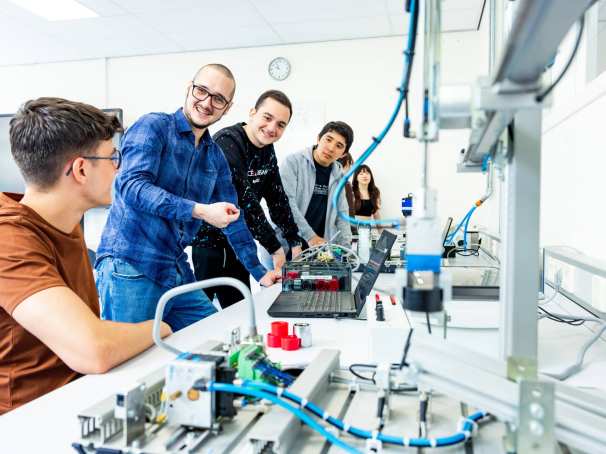 Docent en studenten elektrotechniek aan een Programmable Logic Controller (PLC).