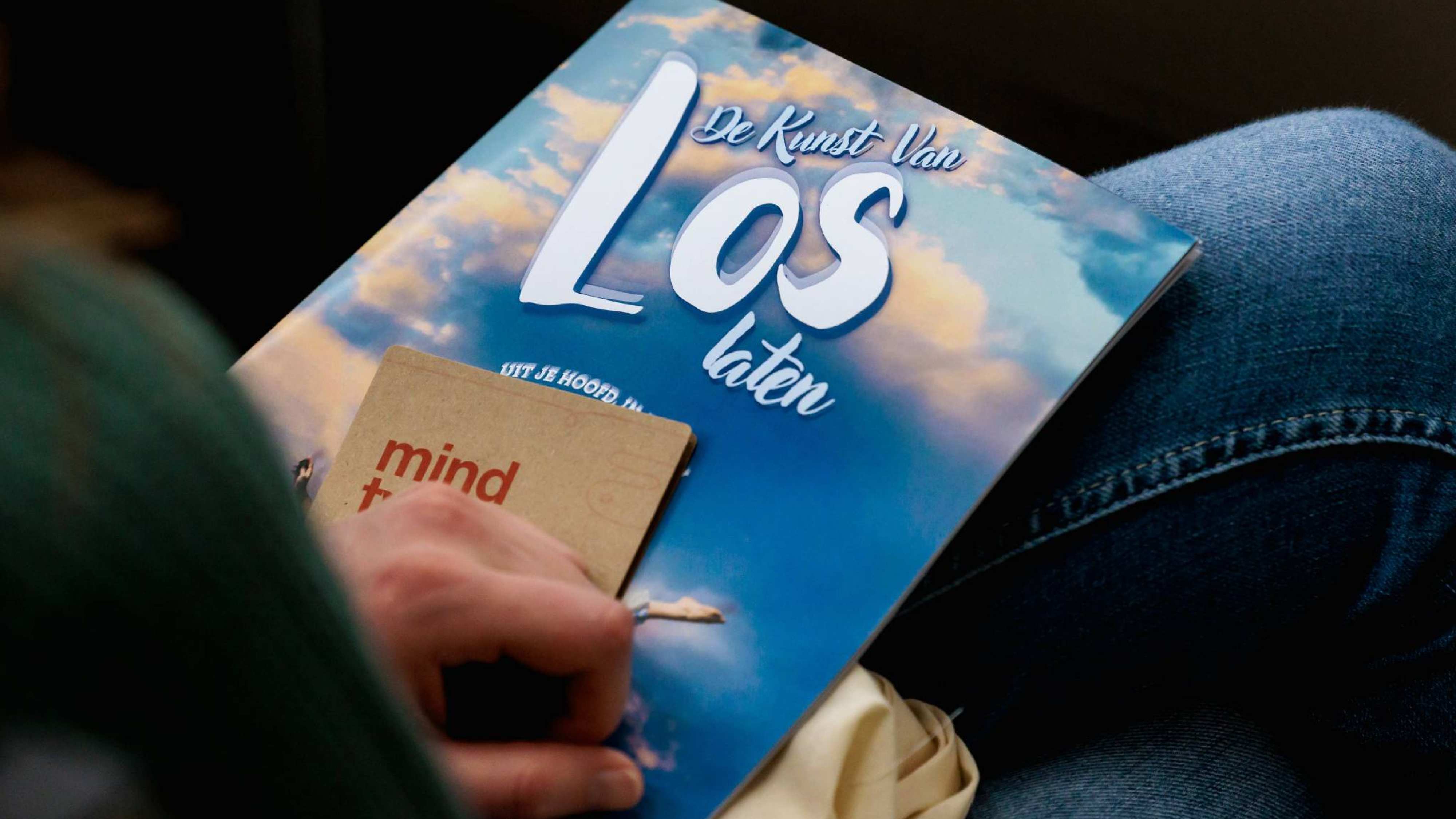 Het boekje wat de deelnemers van festival LOS kregen met een blauwe achtergrond en in witte letters de tekst de kunst van het los laten