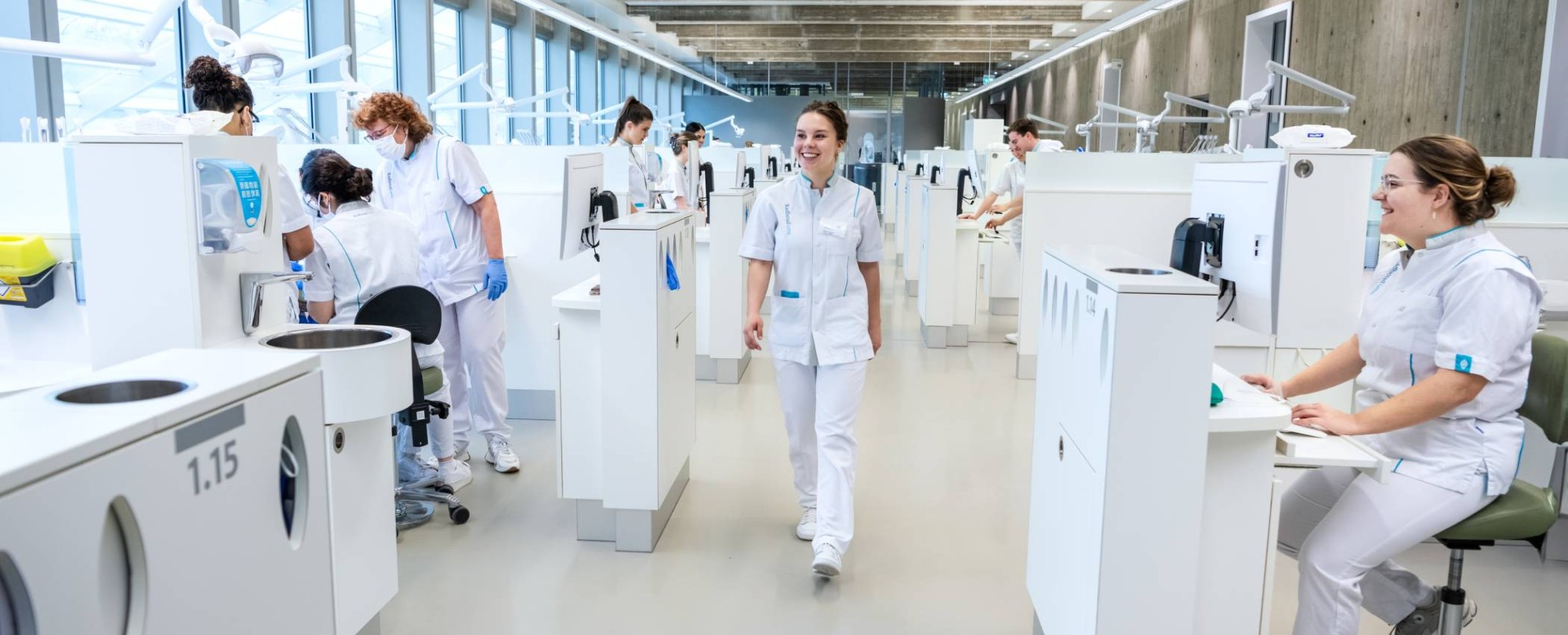 Student lacht en loopt door een drukke kamer vol behandelstoelen.