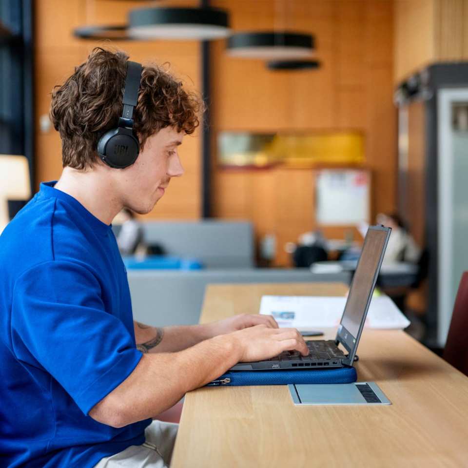 Student met koptelefoon werkt achter computer.