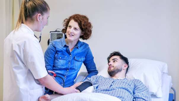 Een student Verpleegkunde meet onder toeziend oog van een docent de bloeddruk bij een medestudent.