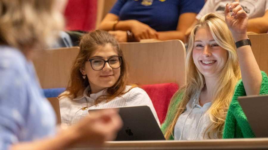 Studente steekt hand op tijdens hoorcollege in de collegezaal