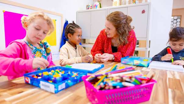 Omscholer naar basisonderwijs legt iets uit aan een kleuter in de klas.