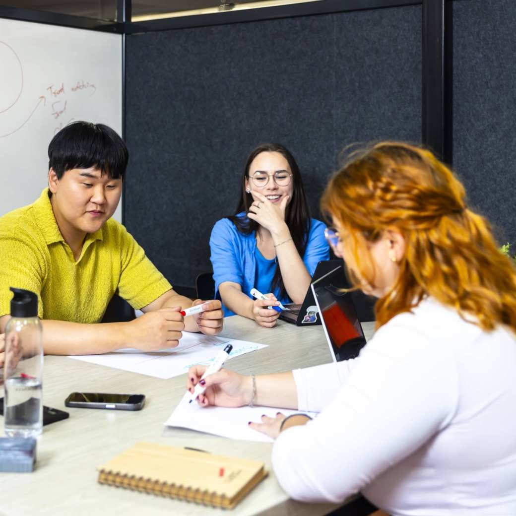 4 studenten overleggen aan tafel met een whiteboard erachter.