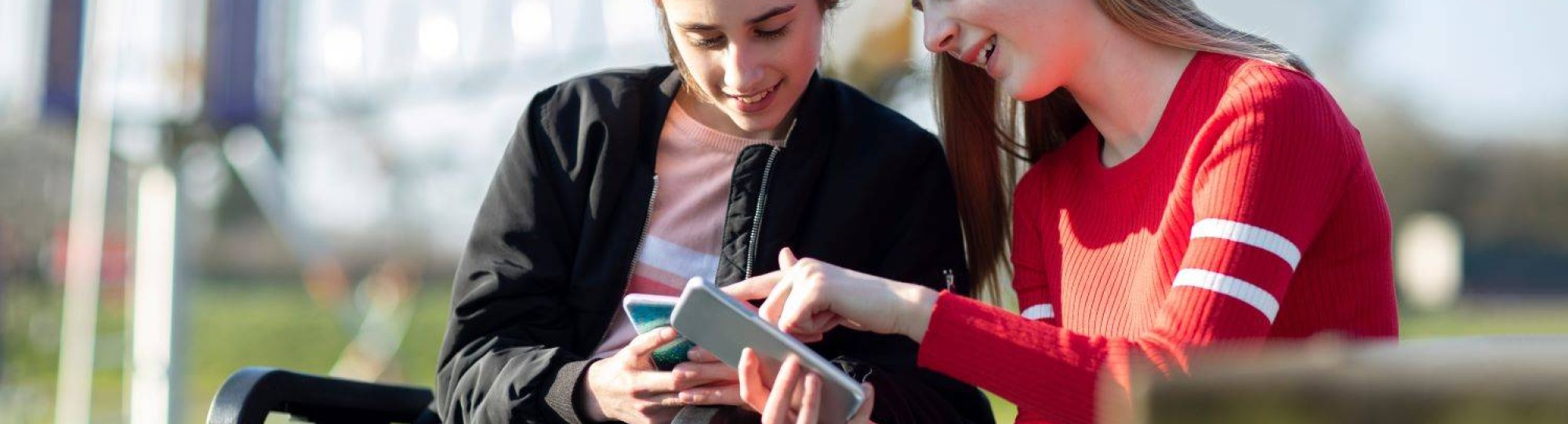 Tiener meisje in rolstoel kijkt naar mobiel met vriendin