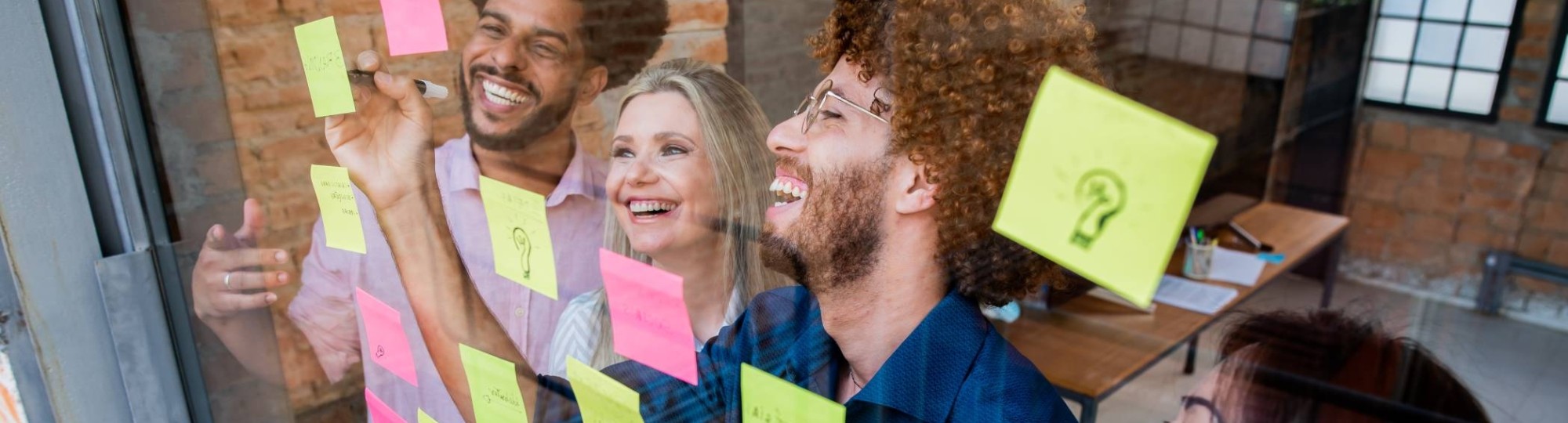 Groep jonge mensen plakken post-its op een glazen wand in een kantoor
