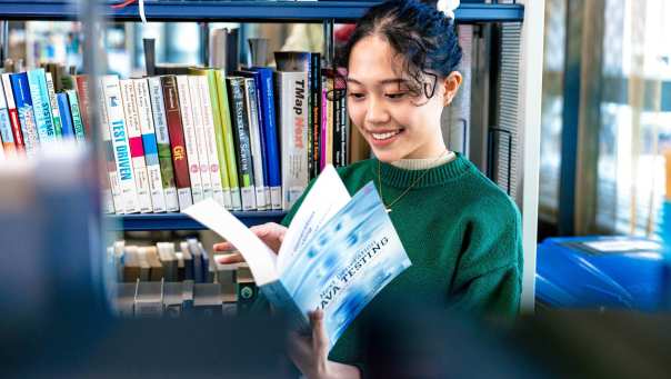 International student Tam browsing through study books in the library on the Arnhem campus of HAN University of Applied Sciences.