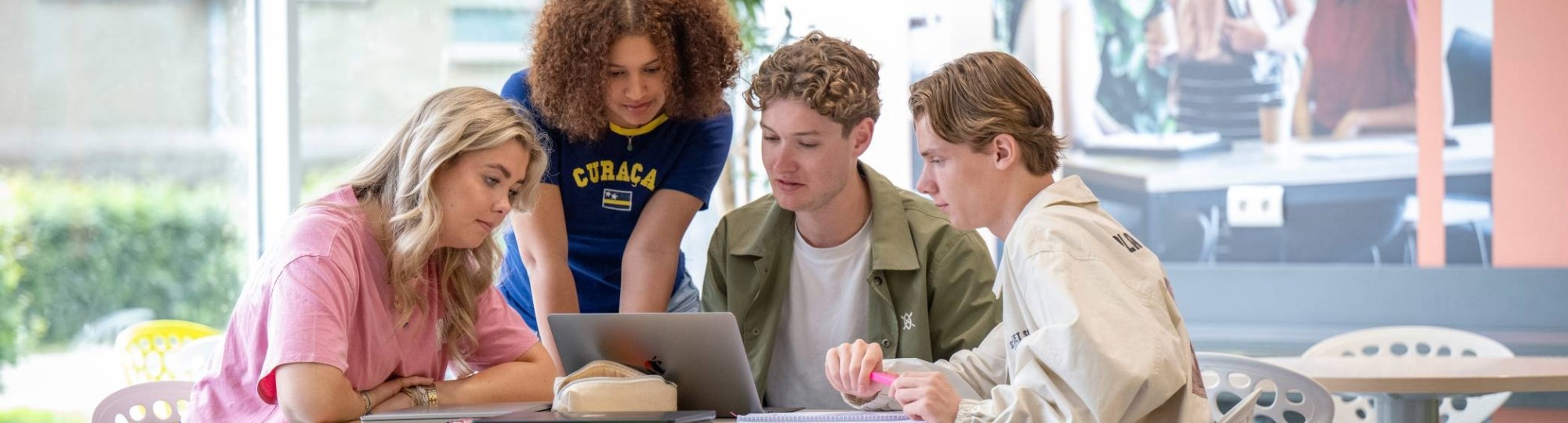 Groepje studenten werken samen aan een ronde tafel in de gang, werkplek in LvS10. Kijken samen naar de laptop.