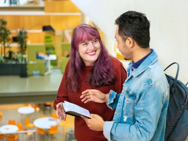 Twee studenten vertellen met elkaar terwijl de een een kladje in de hand heeft met geschreven tekst.
