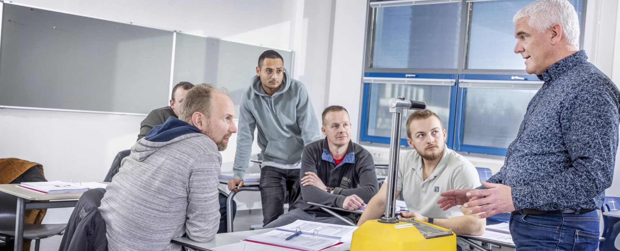 cursisten asfaltwegenbouwlaborant in klas met geel beton apparaat en docent