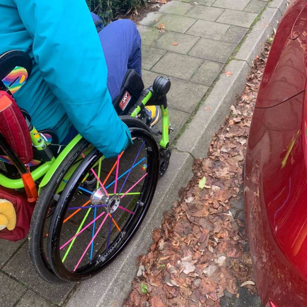 Foto van student in een rolstoel, op weg naar de campus. Hij rijdt op een te smalle stoep.