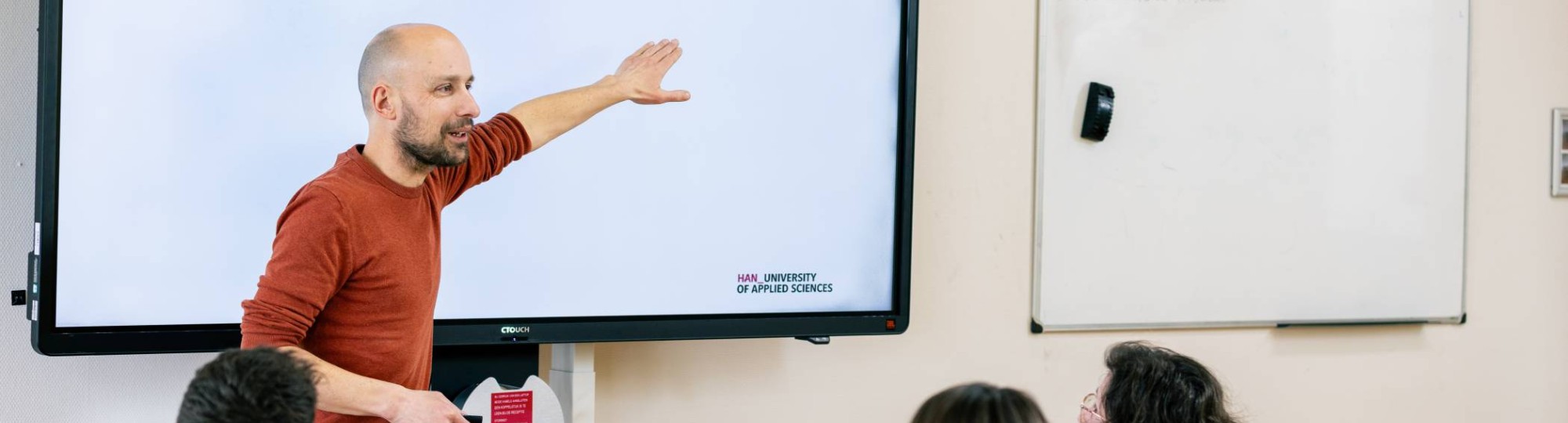 Vier studenten zitten met de laptops opengeklapt te werken aan een tafel en wisselen ideeën uit.