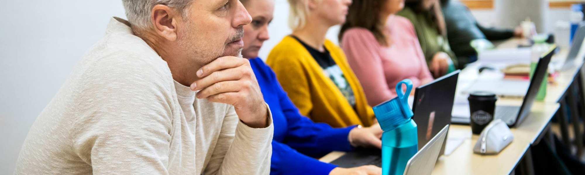 Foto van Master Ontwerpen van Eigentijds Leren. Close-up van één masterstudent die gefocust kijkt met andere masterstudenten vaag op de achtergrond. 