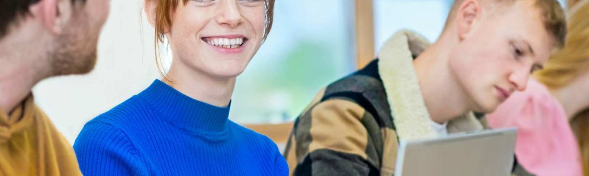 Vier studenten zitten op een rij. Een student specifiek is scherp in beeld en ze lacht naar de persoon naast haar.