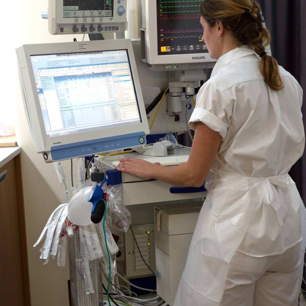 Intensive Care Verpleegkundige kijkt op een verrolbaar scherm met patiëntgegevens.