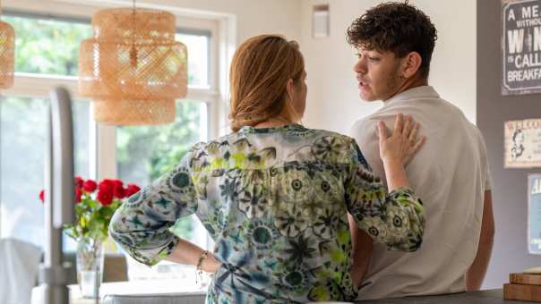 Een moeder legt ter geruststelling een hand op de schouder van haar zoon in de keuken. 