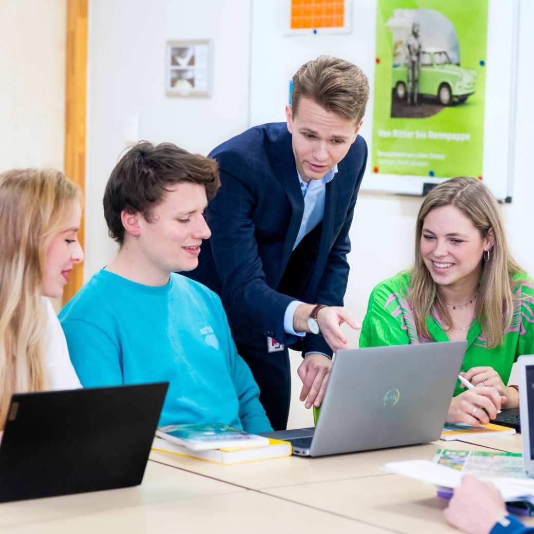 Docent legt drie studenten aan de tafel iets uit.