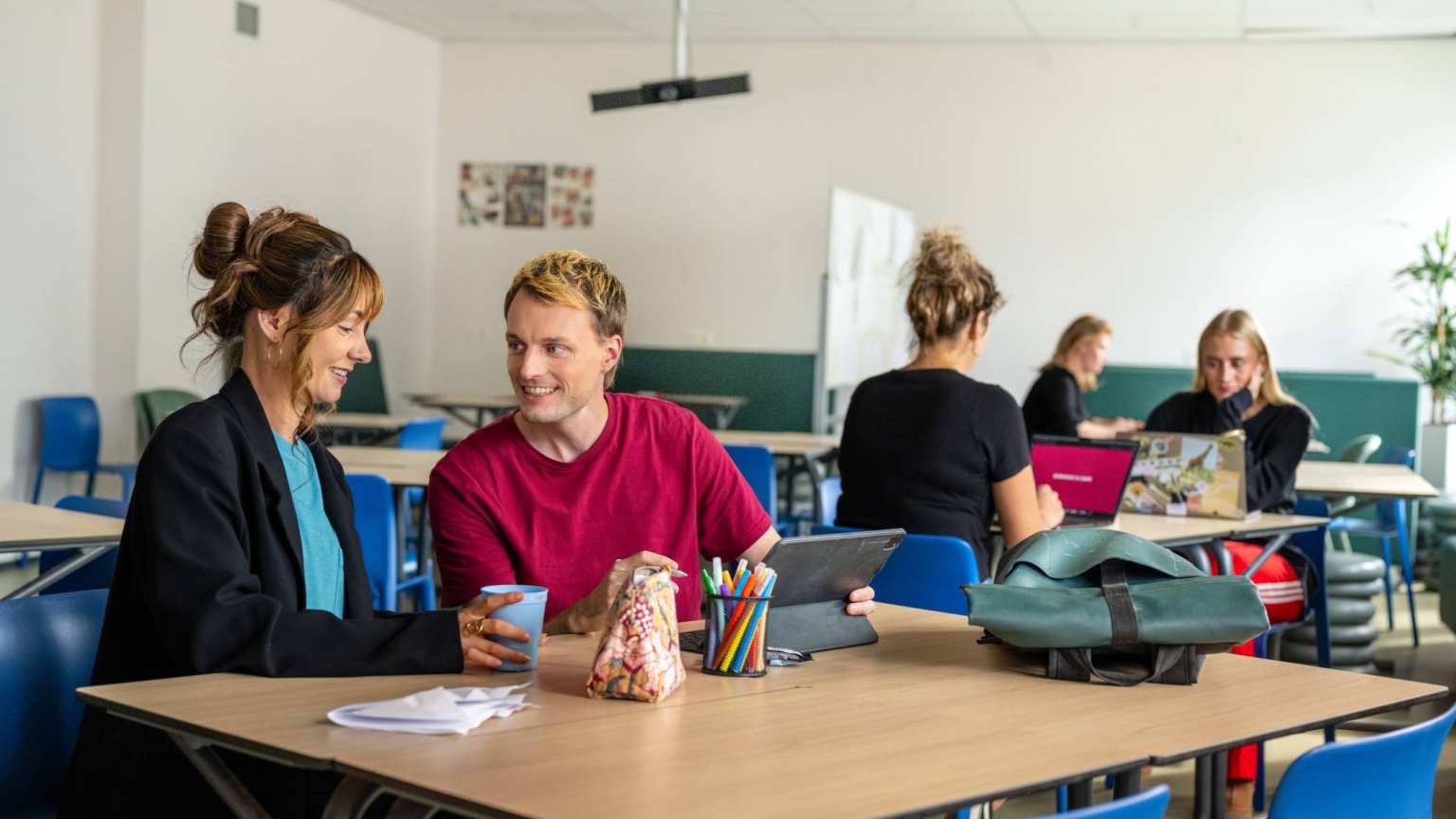 Studenten in klaslokaal aan het werk op laptops en lachen onderling