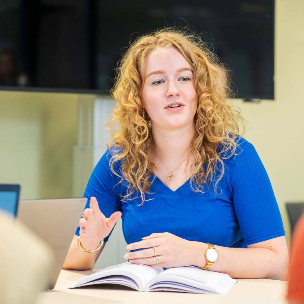 Bachelorstudent met studieboek in gesprek met klasgenoten.