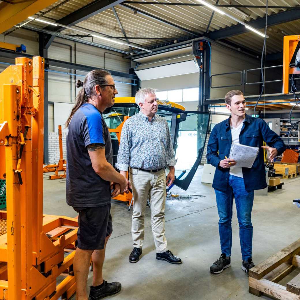 Technische Bedrijfskunde student overlegt met werkplekbegeleider en medewerker op de werkvloer.