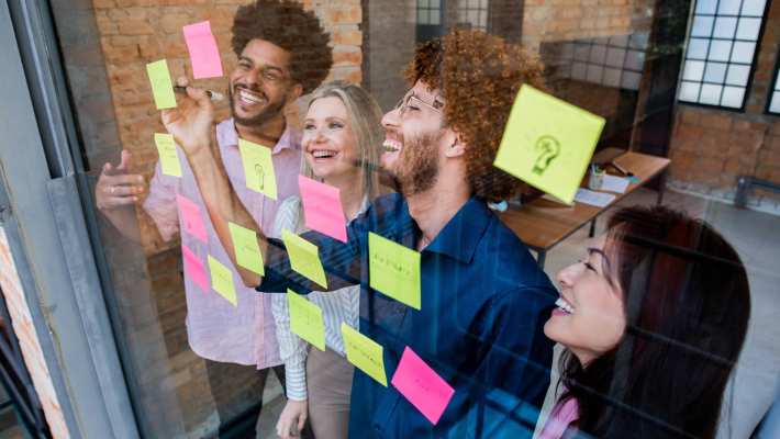 Groep jonge mensen plakken post-its op een glazen wand in een kantoor
