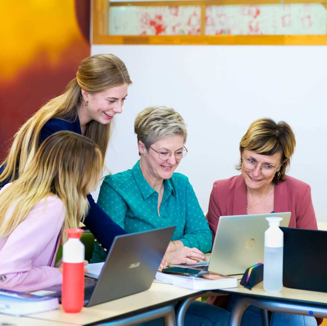 Vier studenten kijken samen op één scherm, terwijl iedereen een laptop heeft.