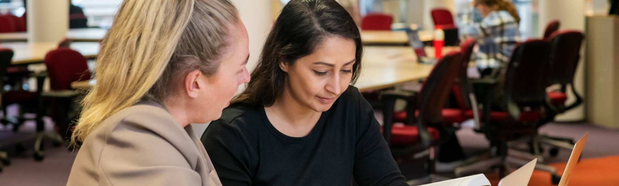 Twee studenten aan het werk in de bibliotheek en kijken naar een boek voor studie PMT deeltijd