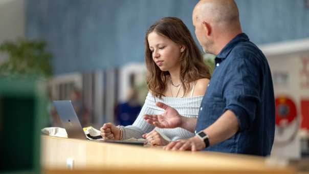 Een docent heeft een gesprek met een student in de hal van gebouw R26, studentbegeleiding. 