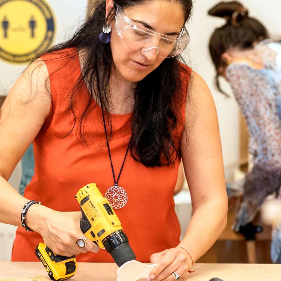 Studente Beeldende therapie gebruikt een boor in het houtlokaal tijdens een praktijkles